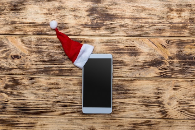 Smartphone con gorro de Papá Noel en el escritorio de madera