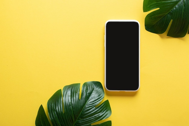 Smartphone y hojas de Monstera Deliciosa sobre un fondo amarillo con un lugar para la masa Blogger en verano Copiar espacio Vista superior plana