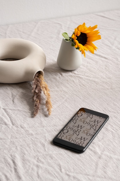 Smartphone con imagen de letras y símbolos en pantalla, pequeño girasol en vidrio cerámico y creativo jarrón blanco en forma de anillo con picos secos