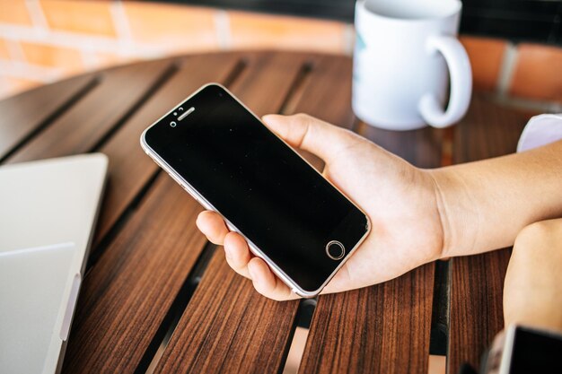 Smartphone in der Hand mit Tisch und Becher