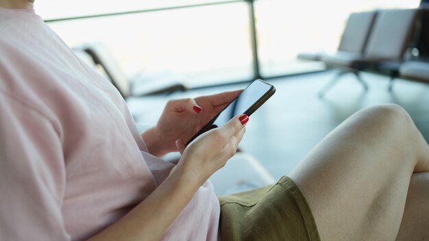 Smartphone in weiblichen Händen im Wartezimmer des Flughafens oder Bahnhofs