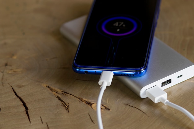 Smartphone-Ladebatterie von einer externen Powerbank im Freien. Hölzerner Hintergrund.