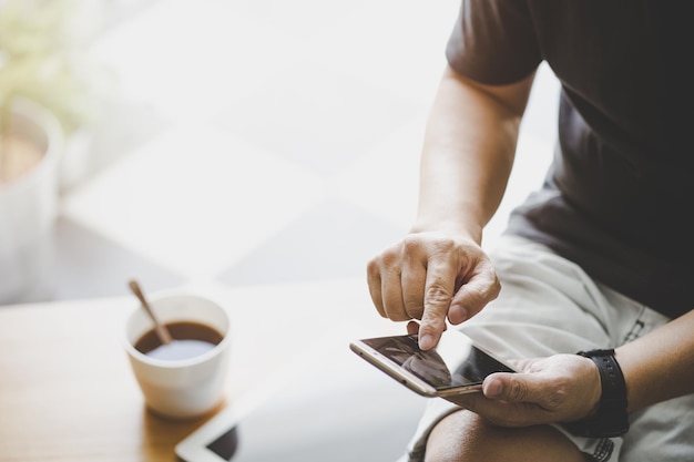 Smartphone en mano de hombre joven con tableta digital y café