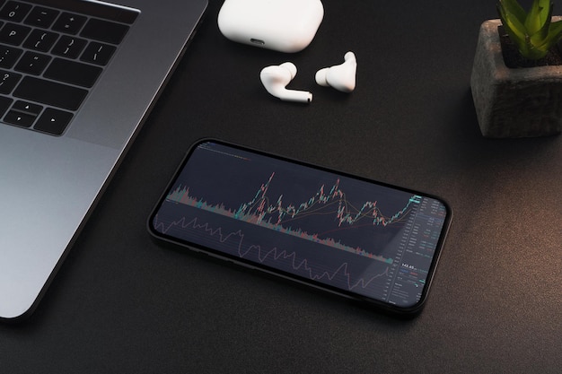 Smartphone mit Finanzbörsendiagramm auf dem Bildschirm auf schwarzem Hintergrundtisch Büroumgebung Börse