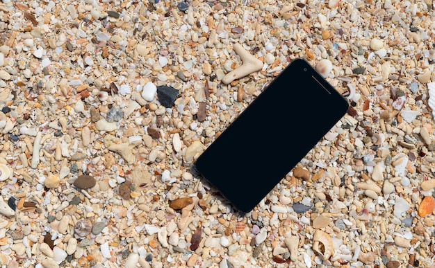 Smartphone mit leerem Bildschirm auf tropischem Sandstrandhintergrund