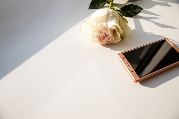 Smartphone mit leerem Bildschirm, umgeben von blühender Rosenblume.