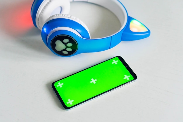 Smartphone mit leerem Greenscreen-Modell mit drahtlosen Kinderkopfhörern isoliert auf grauem Hintergrund