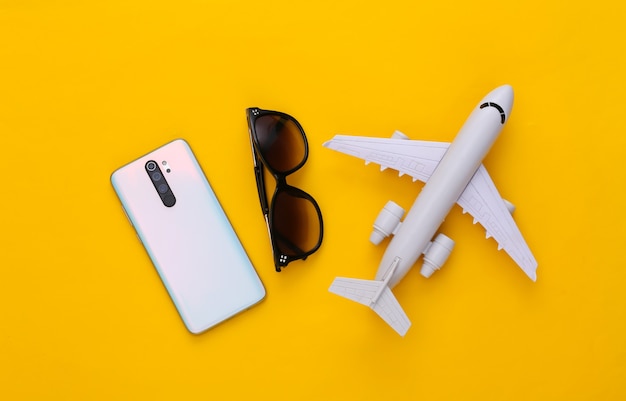 Smartphone moderno, avión y gafas de sol en amarillo. Concepto de viaje