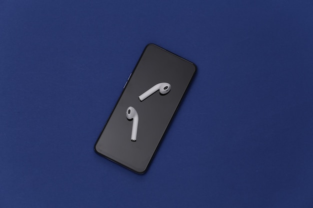 Foto smartphone moderno com fones de ouvido sem fio no fundo azul clássico.