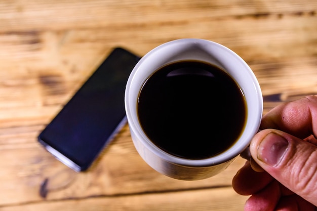 Smartphone moderno com tela em branco sobre fundo de madeira e mão com xícara de café