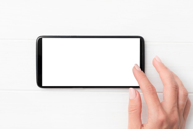 Smartphone moderno negro con pantalla en blanco en las manos sobre fondo blanco de mesa