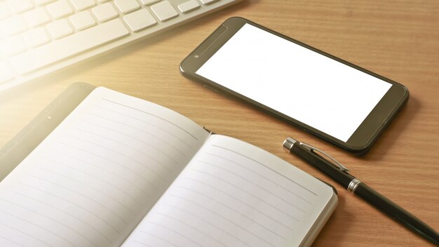 Smartphone móvel com tela branca e notebook memo na mesa de trabalho