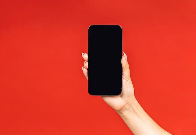 Smartphone na mão feminina isolado em fundo vermelho foto aproximada do telefone móvel