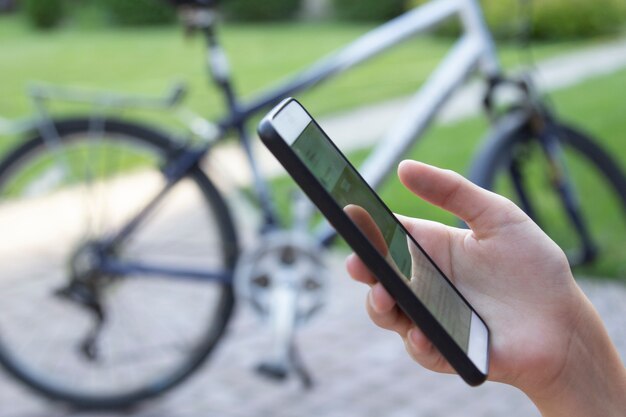 Smartphone na mão mulher no fundo da bicicleta turva. Rede de comunicação móvel.