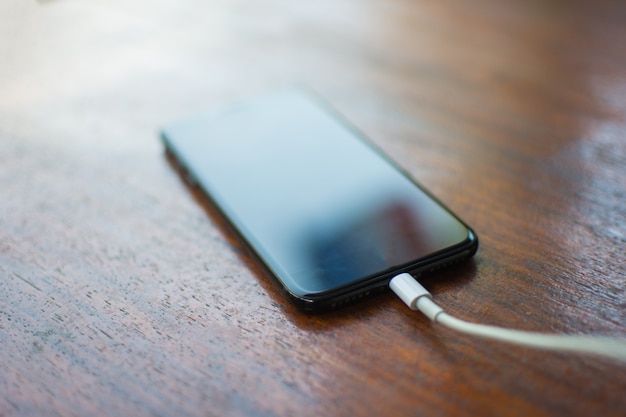 Smartphone negro con cable de carga en mesa de madera.