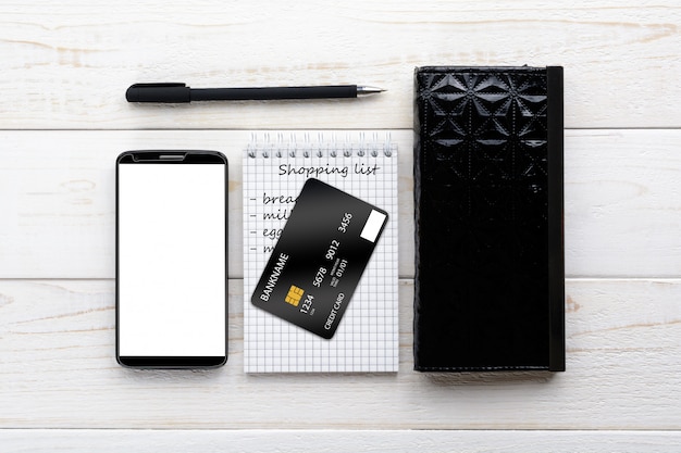 Smartphone, Notebook, Stift und Kreditkarte auf einem weißen Tisch