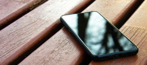 Foto smartphone con la pantalla apagada en un banco smartphone negro en la calle un fondo de madera