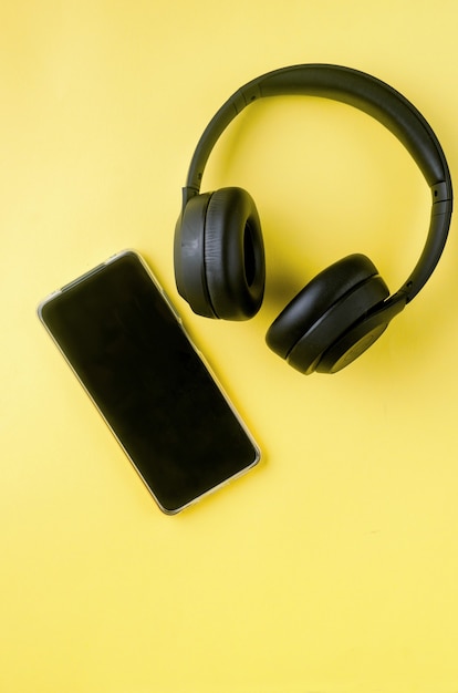 Smartphone con pantalla en blanco con auriculares en papel amarillo Vista superior de fondo. Concepto escuchar música, emitir, audio desde un teléfono inteligente.