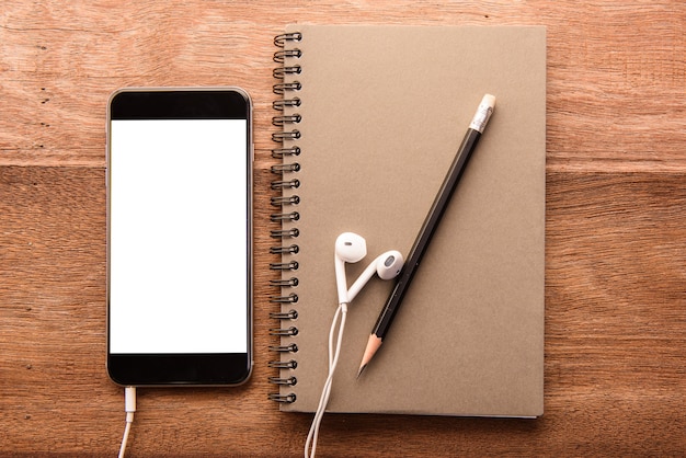 Smartphone con pantalla en blanco y el cuaderno en la mesa de madera con Copyspace
