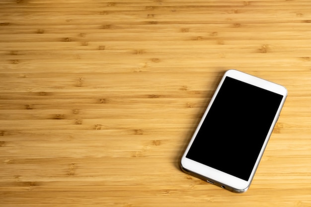 Smartphone con pantalla en blanco en la mesa de madera de bambú en la oficina