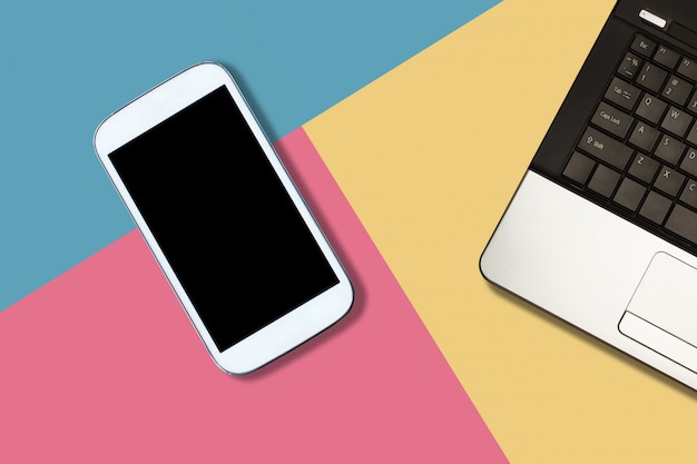 Smartphone con pantalla en blanco y portátil sobre fondo de color pastel