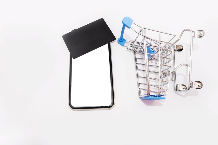 Foto smartphone con pantalla en blanco y una tarjeta de crédito negra en la parte superior, y un carrito de compras sobre fondo blanco.