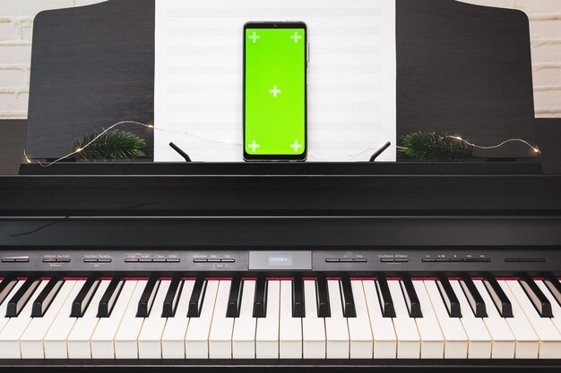 Smartphone con pantalla verde en un piano electrónico con partituras y iluminación Lección de piano en línea Concierto o conferencia de vacaciones de música en línea Mockup para aplicaciones de música móviles Educación musical en línea