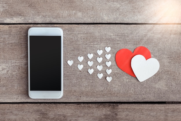 Smartphone y papel de corazones sobre fondo de madera