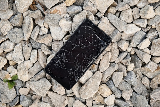 Smartphone preto com tela quebrada nas pedras