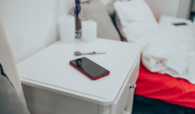 Smartphone preto em uma caixa vermelha na mesa de cabeceira. Relógio feminino na mesa do quarto no contexto da cama. Fechar-se