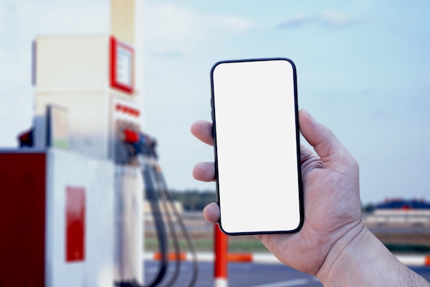 smartphone en primer plano de la mano en el fondo de una gasolinera. Pago repostaje online.