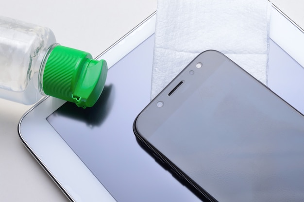 Smartphone y tableta con una botella de gel desinfectante y una servilleta. tratamiento antiviral y antibacteriano de dispositivos portátiles.