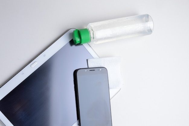 Smartphone y tableta en el lugar con una botella de gel desinfectante y servilleta. tratamiento antiviral y antibacteriano de dispositivos portátiles.