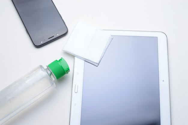 Smartphone y tableta sobre un fondo blanco en el lugar con una botella de gel desinfectante y servilleta. tratamiento antiviral y antibacteriano de dispositivos portátiles.