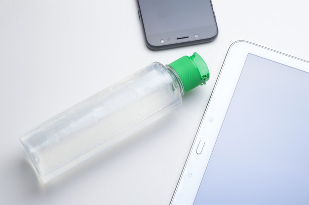 Smartphone y tableta sobre un fondo blanco en el lugar con una botella de gel desinfectante y servilleta. tratamiento antiviral y antibacteriano de dispositivos portátiles.