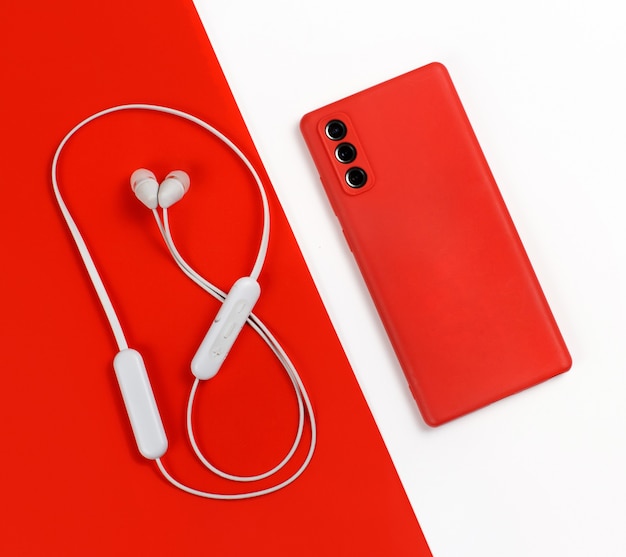 Foto smartphone con tapa roja y vista superior de auriculares inalámbricos blancos sobre fondo rojo y blanco