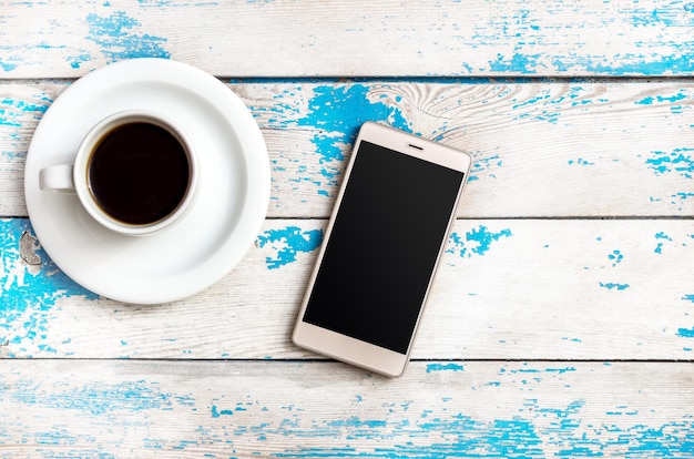 Smartphone con taza de café en el fondo de madera.