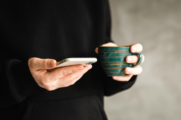 Smartphone y taza de café hecha a mano en las manos de un hombre primer plano el concepto de usar la tecnología