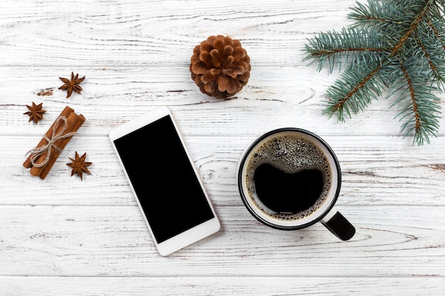 Smartphone con taza de café en la mesa de madera rama de árbol de navidad y decoración navideña