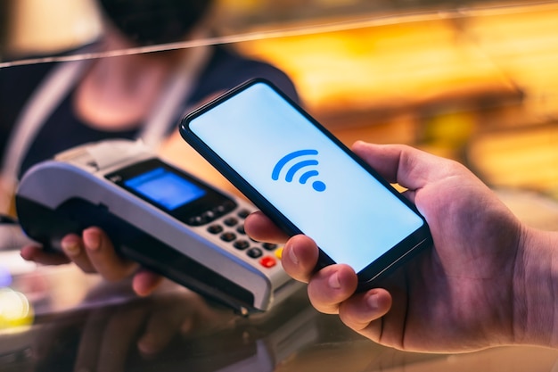 Smartphone en tienda con tecnología NFC con el terminal de pago al fondo