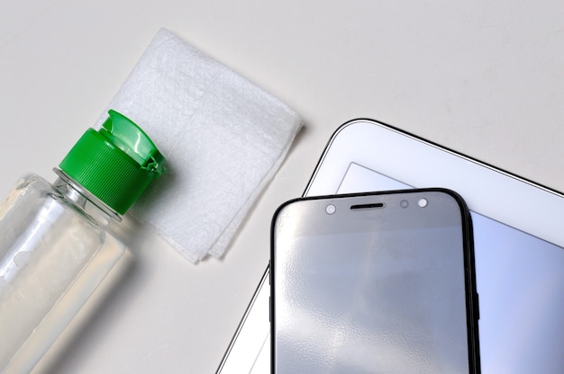 Smartphone und Tablet an Ort und Stelle mit einer Flasche Gel-Desinfektionsmittel und Serviette. antivirale und antibakterielle Behandlung von tragbaren Geräten.