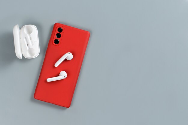 Smartphone vermelho e fones de ouvido sem fio na vista superior do plano de fundo cinza