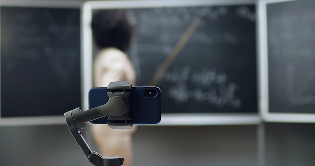 Smartphone-Videoaufzeichnung in der Schule. Online-Lernen. Afroamerikanische junge Lehrerin, die Mathematik- oder Physikformeln im Unterricht erklärt. Quarantänekonzept. Studie während des Coronavirus.