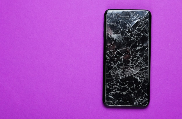 Foto smartphone con vidrio protector roto en mesa púrpura. vista superior