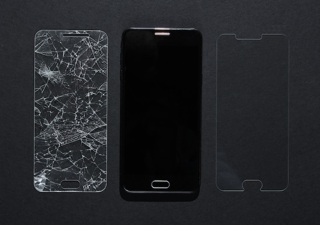 Foto smartphone con vidrio protector roto y nuevo en mesa negra. vista superior