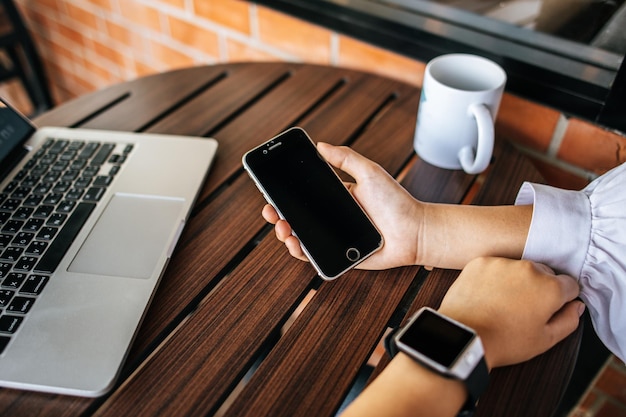 Smartphone zur Hand mit Tisch und Laptop