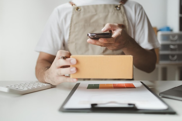 Smartphones werden verwendet, um verschiedene Aktivitäten durchzuführen, um den Verkauf an Geschäfte zu fördern. Der Besitzer eines Online-Shops verpackt Produkte in Paketkisten auf der Grundlage von Bestellungen von Online-Verkaufsstellen.