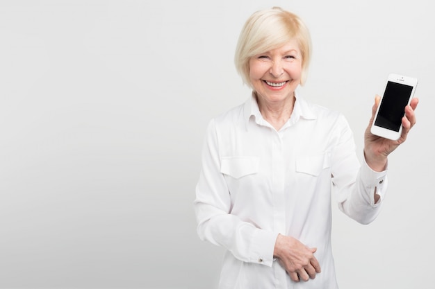 Smiley ältere Frau hält ein neues Smartphone in der Hand. Sie hat gelernt, wie man es benutzt. Sie ist begeistert von Internet und neuen Technologien.