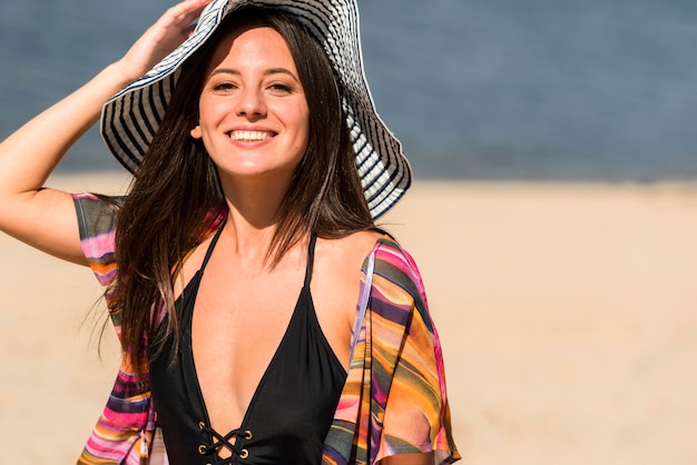 Smiley-Frau, die am Strand mit Hut aufwirft