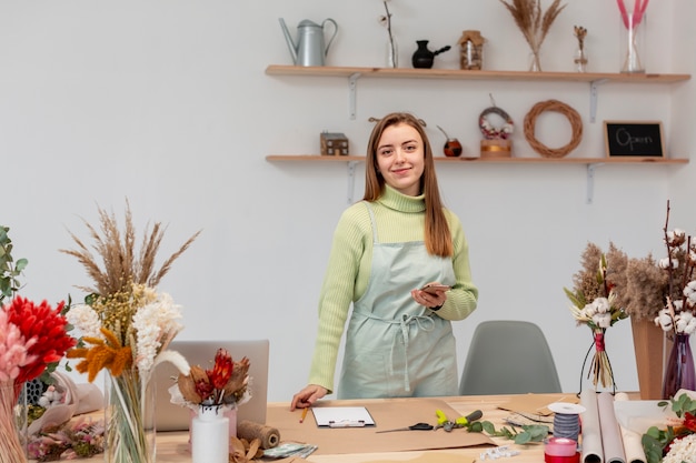 Smiley-Frau, die an einem Blumenladen arbeitet, der durch Pflanzen umgeben ist